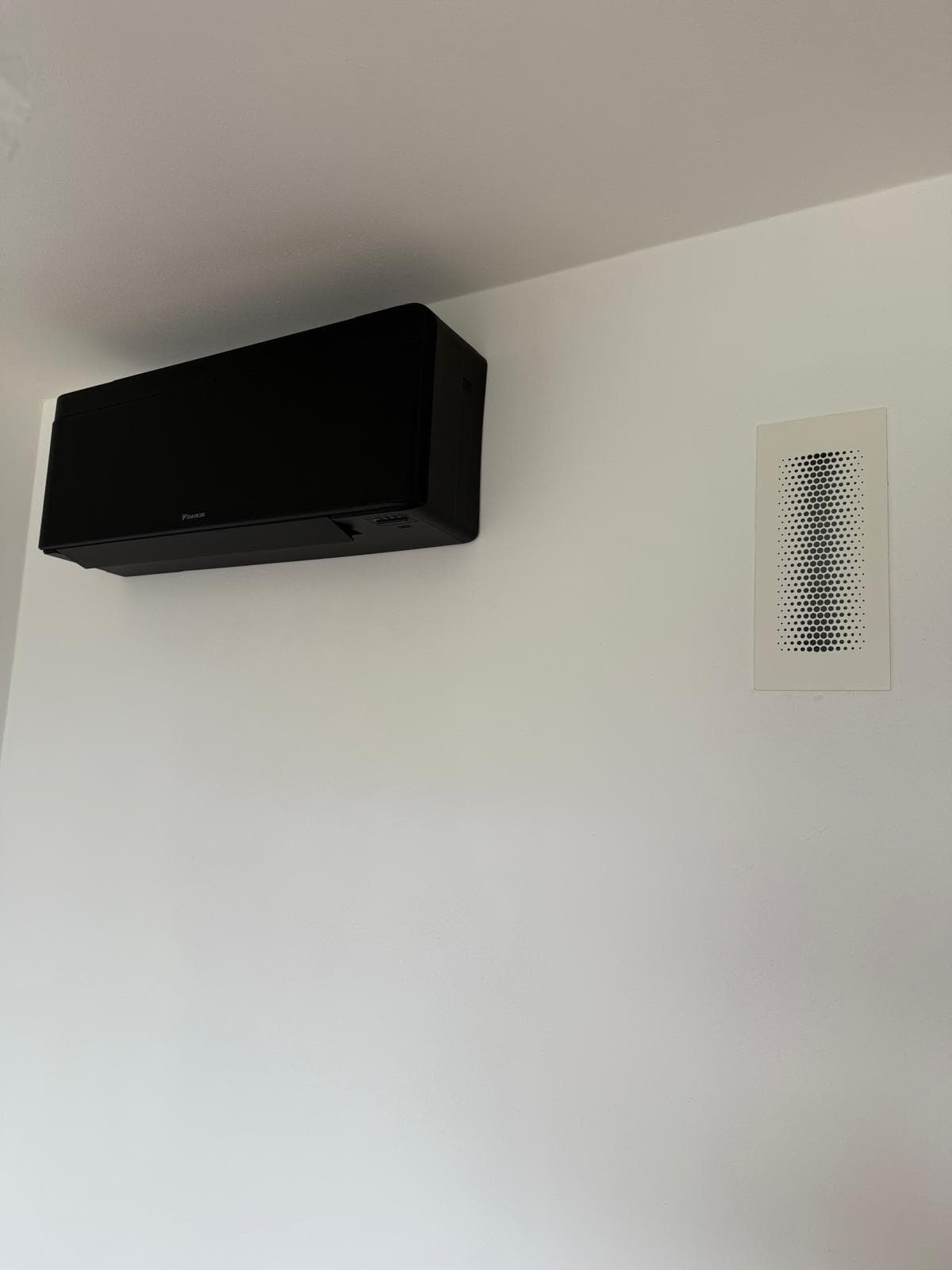 Schwarze Daikin Stylish Inneneinheit an der Wand, neben einem Lüftungsgitter